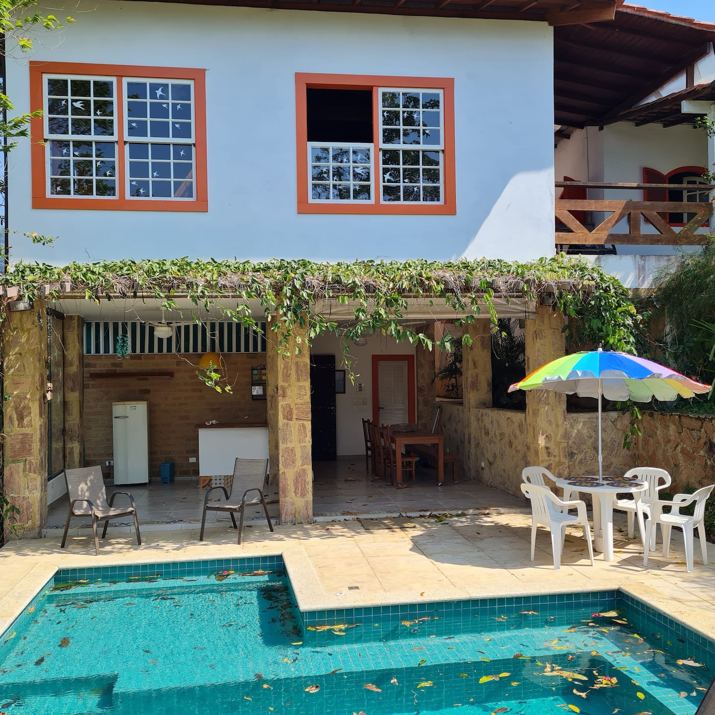 Fachada branca da Casa Linda com janelas vermelhas e piscina